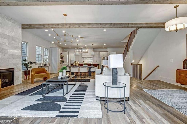 living room with light wood finished floors, an inviting chandelier, a tiled fireplace, and beam ceiling