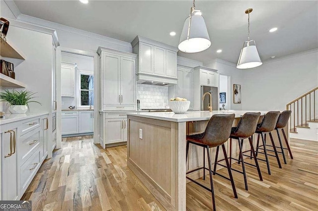 kitchen featuring crown molding, tasteful backsplash, a kitchen breakfast bar, a kitchen island with sink, and light wood-style floors