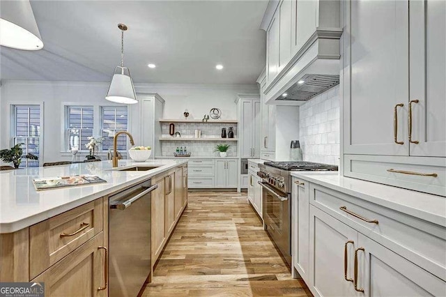 kitchen with light countertops, open shelves, stainless steel appliances, a sink, and wall chimney range hood