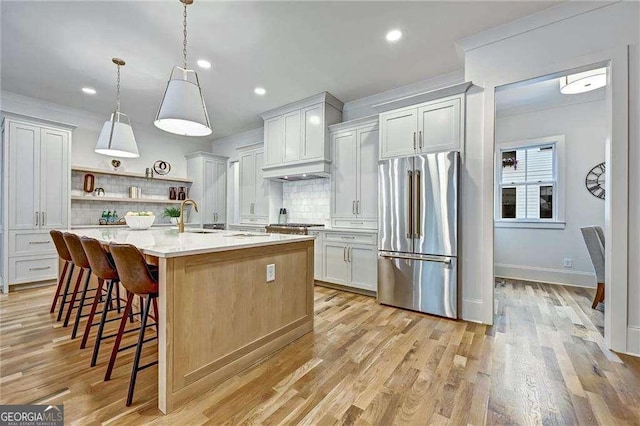 kitchen featuring light countertops, a sink, open shelves, light wood-type flooring, and freestanding refrigerator
