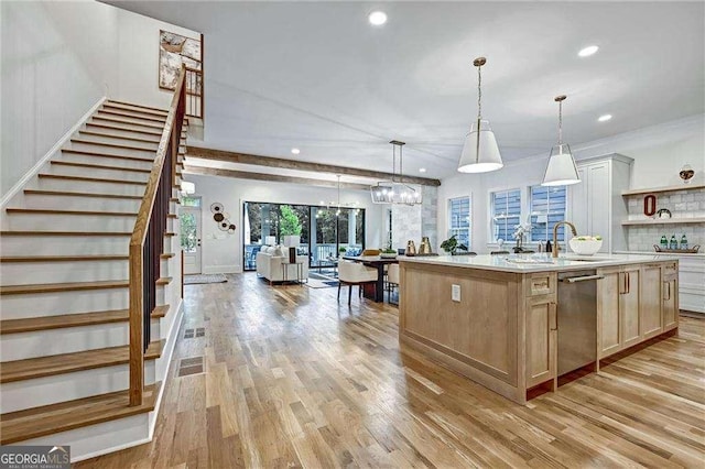 kitchen with open floor plan, light countertops, stainless steel dishwasher, an island with sink, and light wood-style flooring