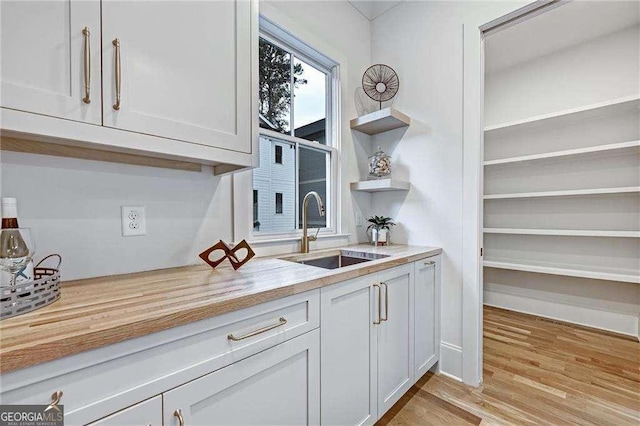 kitchen featuring white cabinets, light wood-style flooring, a sink, and open shelves