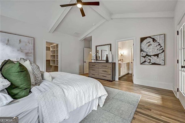 bedroom with baseboards, connected bathroom, wood finished floors, vaulted ceiling with beams, and a spacious closet