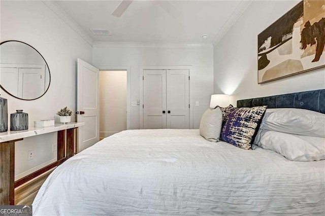 bedroom with crown molding, visible vents, a ceiling fan, a closet, and wood finished floors