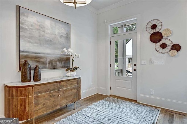 foyer with baseboards, visible vents, crown molding, and wood finished floors
