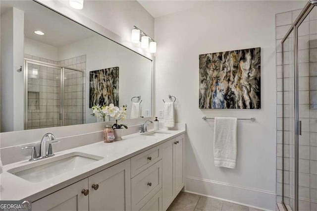full bathroom featuring double vanity, a sink, a stall shower, and baseboards