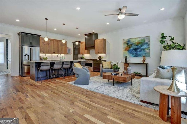 living area featuring a ceiling fan, light wood finished floors, baseboards, ornamental molding, and recessed lighting