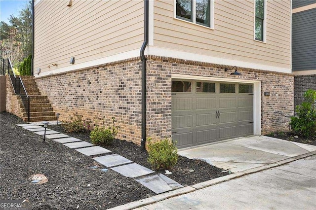 view of side of property featuring driveway, an attached garage, stairway, and brick siding