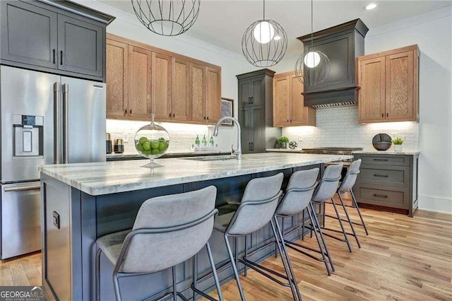 kitchen with built in refrigerator, light stone countertops, crown molding, and light wood-style floors