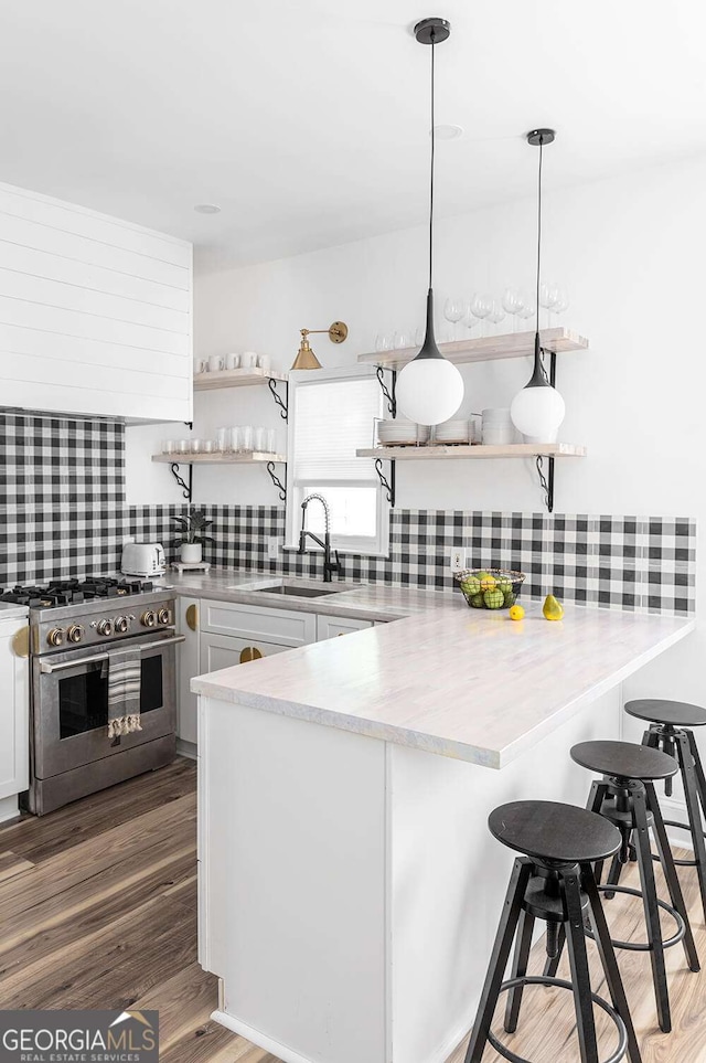 kitchen featuring open shelves, high end stainless steel range oven, a sink, wood finished floors, and a peninsula