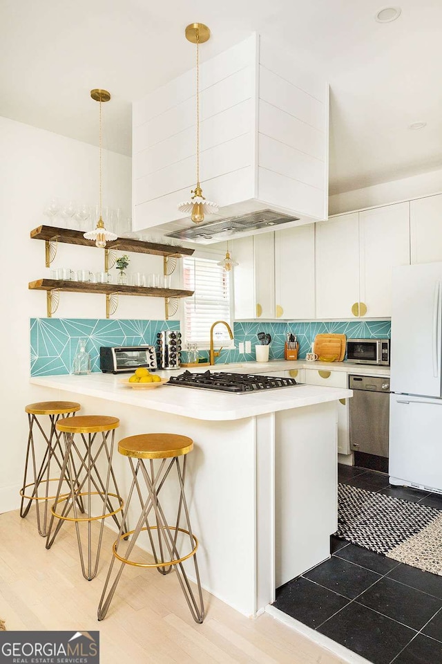 kitchen with a kitchen bar, white cabinets, backsplash, and appliances with stainless steel finishes