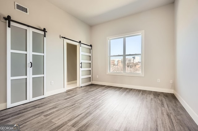 unfurnished bedroom featuring a barn door, wood finished floors, visible vents, and baseboards
