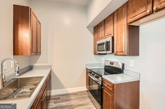 kitchen featuring brown cabinets, a sink, stainless steel appliances, light wood-style floors, and baseboards