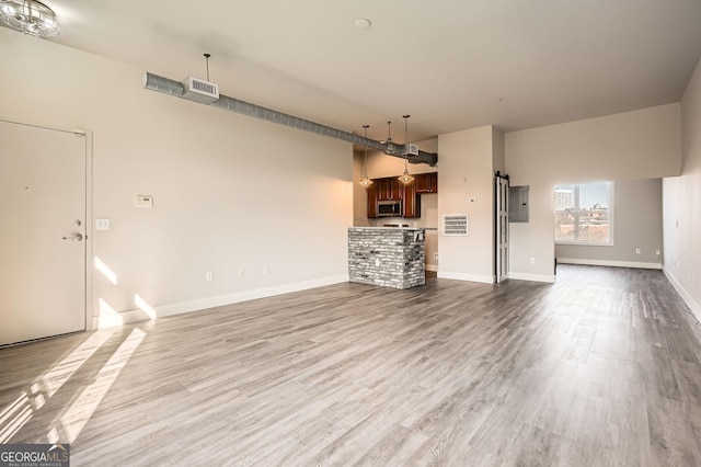unfurnished living room featuring electric panel, visible vents, baseboards, and wood finished floors
