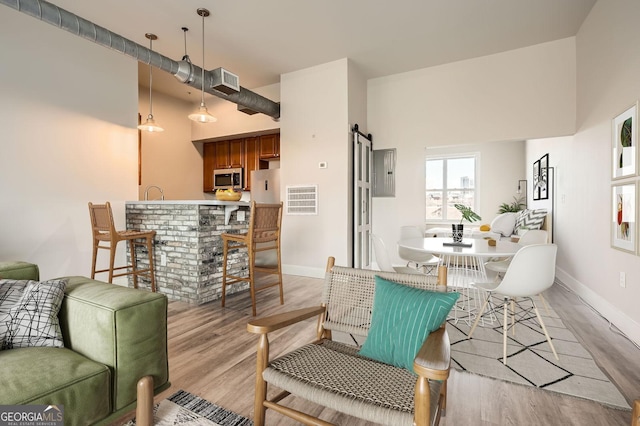 living area with a barn door, baseboards, light wood-type flooring, and visible vents