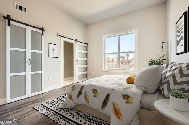 bedroom featuring visible vents, baseboards, a barn door, and wood finished floors
