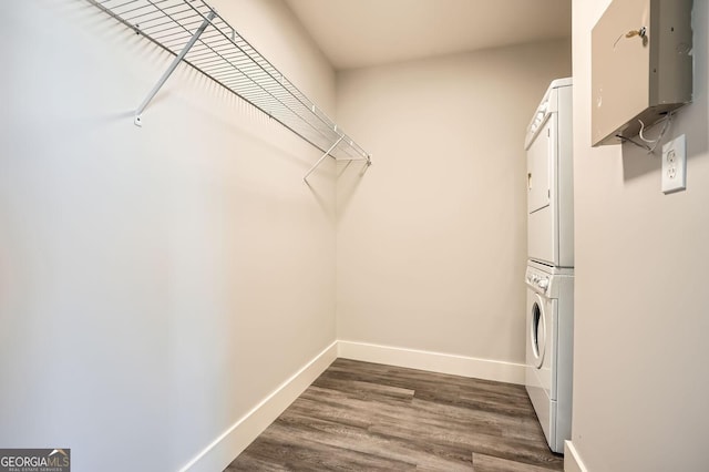 laundry room featuring stacked washer / dryer, laundry area, baseboards, and dark wood-style flooring