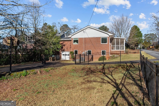 rear view of house featuring a sunroom, a yard, aphalt driveway, brick siding, and fence private yard