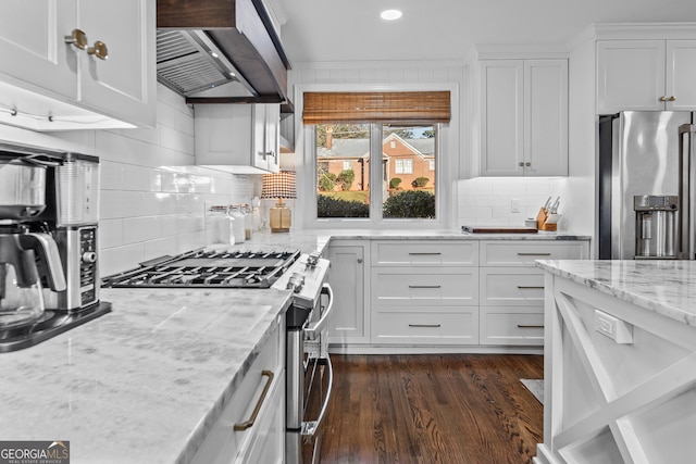 kitchen with light stone countertops, white cabinetry, stainless steel appliances, extractor fan, and backsplash