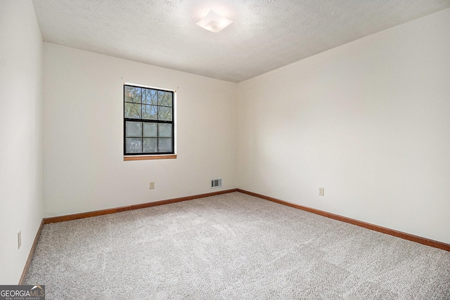 empty room with carpet flooring, a textured ceiling, baseboards, and visible vents