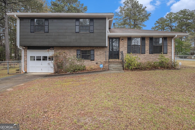 tri-level home featuring a front lawn, brick siding, fence, and a garage