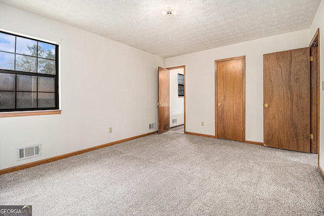 unfurnished bedroom featuring a textured ceiling, multiple closets, baseboards, visible vents, and carpet