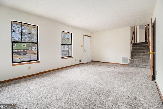 unfurnished living room with a textured ceiling, visible vents, baseboards, stairway, and carpet floors