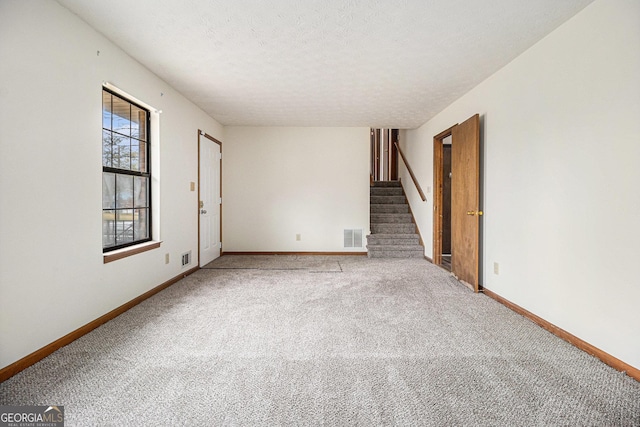 carpeted empty room with a textured ceiling, baseboards, stairs, and visible vents