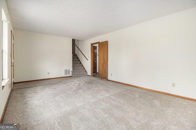 carpeted empty room featuring stairs, visible vents, and baseboards