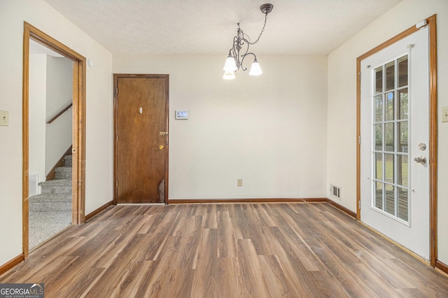 unfurnished dining area featuring stairs, visible vents, wood finished floors, and a chandelier