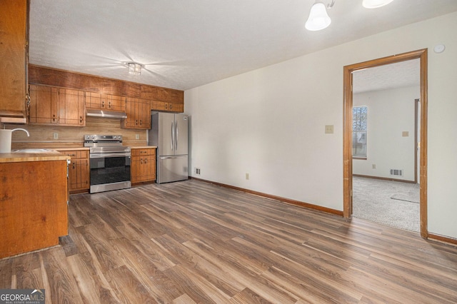 kitchen featuring light countertops, a sink, brown cabinets, under cabinet range hood, and stainless steel appliances