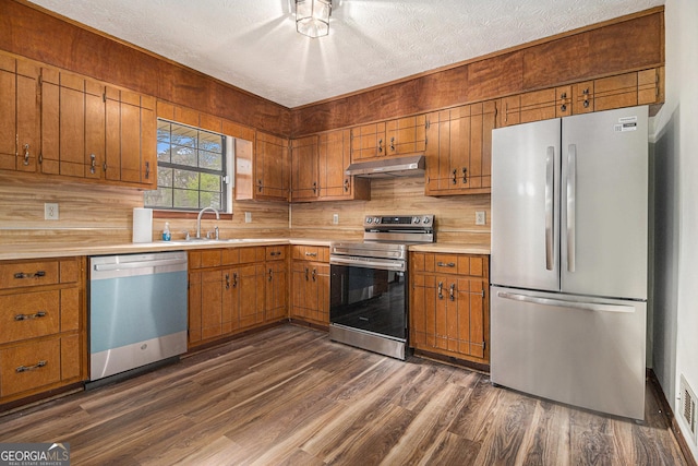 kitchen featuring light countertops, dark wood-style flooring, under cabinet range hood, a sink, and appliances with stainless steel finishes