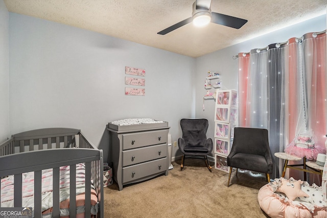 bedroom featuring a textured ceiling, a crib, a ceiling fan, and light carpet