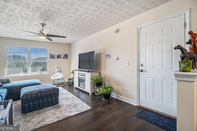 living room with baseboards, a ceiling fan, a textured ceiling, and dark wood-style flooring
