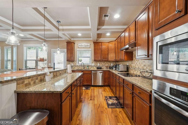kitchen with brown cabinets, hanging light fixtures, light wood-style flooring, stainless steel appliances, and coffered ceiling