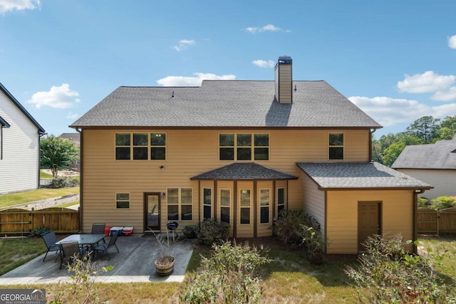 rear view of house with roof with shingles, fence, a chimney, and a patio area