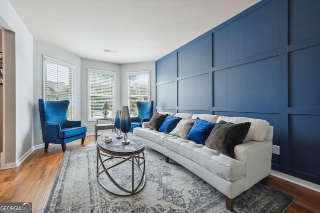 living area with baseboards, a decorative wall, wood finished floors, and visible vents