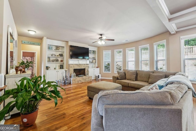 living area with crown molding, a brick fireplace, ceiling fan, and wood finished floors