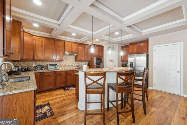 kitchen with a kitchen breakfast bar, a sink, light stone counters, light wood-style floors, and under cabinet range hood