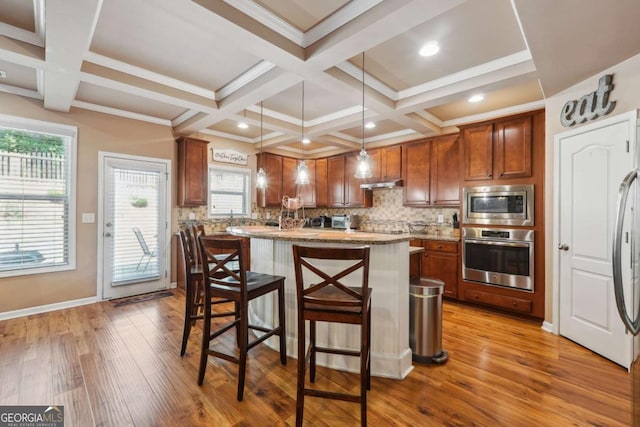 kitchen featuring appliances with stainless steel finishes, wood finished floors, a kitchen breakfast bar, and tasteful backsplash