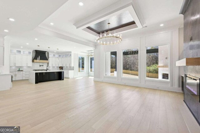 3057 Bold Springs Rd, Dacula, GA 30019 - unfurnished living room with light wood-style flooring, a tray ceiling, a glass covered fireplace, recessed lighting, and an inviting chandelier