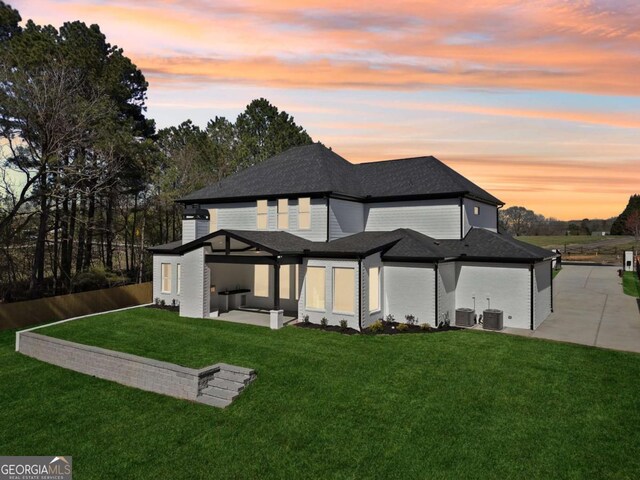 3057 Bold Springs Rd, Dacula, GA 30019 - back of property at dusk featuring a lawn, roof with shingles, concrete driveway, central AC unit, and a patio area