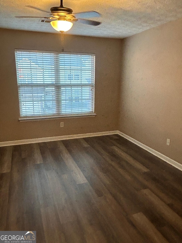empty room with dark wood finished floors, a textured ceiling, baseboards, and ceiling fan