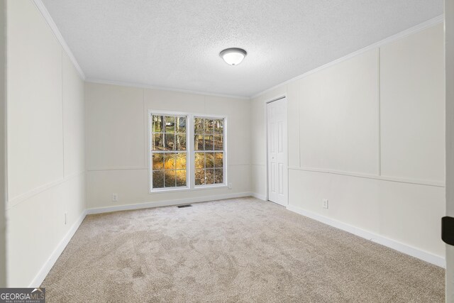 carpeted spare room with crown molding, baseboards, visible vents, and a textured ceiling
