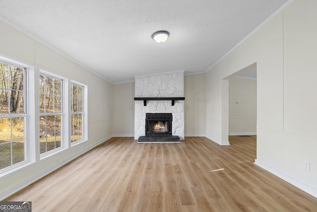 unfurnished living room featuring baseboards, ornamental molding, light wood-style flooring, a fireplace, and a textured ceiling