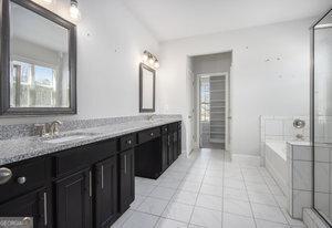 bathroom with tile patterned flooring, a garden tub, double vanity, and a sink