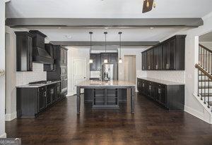 kitchen with tasteful backsplash, dark wood finished floors, light countertops, and a kitchen island with sink