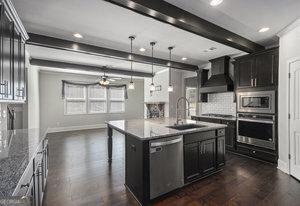 kitchen with dark wood finished floors, a sink, appliances with stainless steel finishes, beamed ceiling, and wall chimney exhaust hood