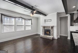 unfurnished living room with baseboards, beam ceiling, a stone fireplace, dark wood-style floors, and a ceiling fan