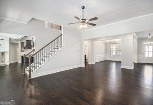 unfurnished living room featuring ornamental molding, wood finished floors, stairway, baseboards, and ceiling fan